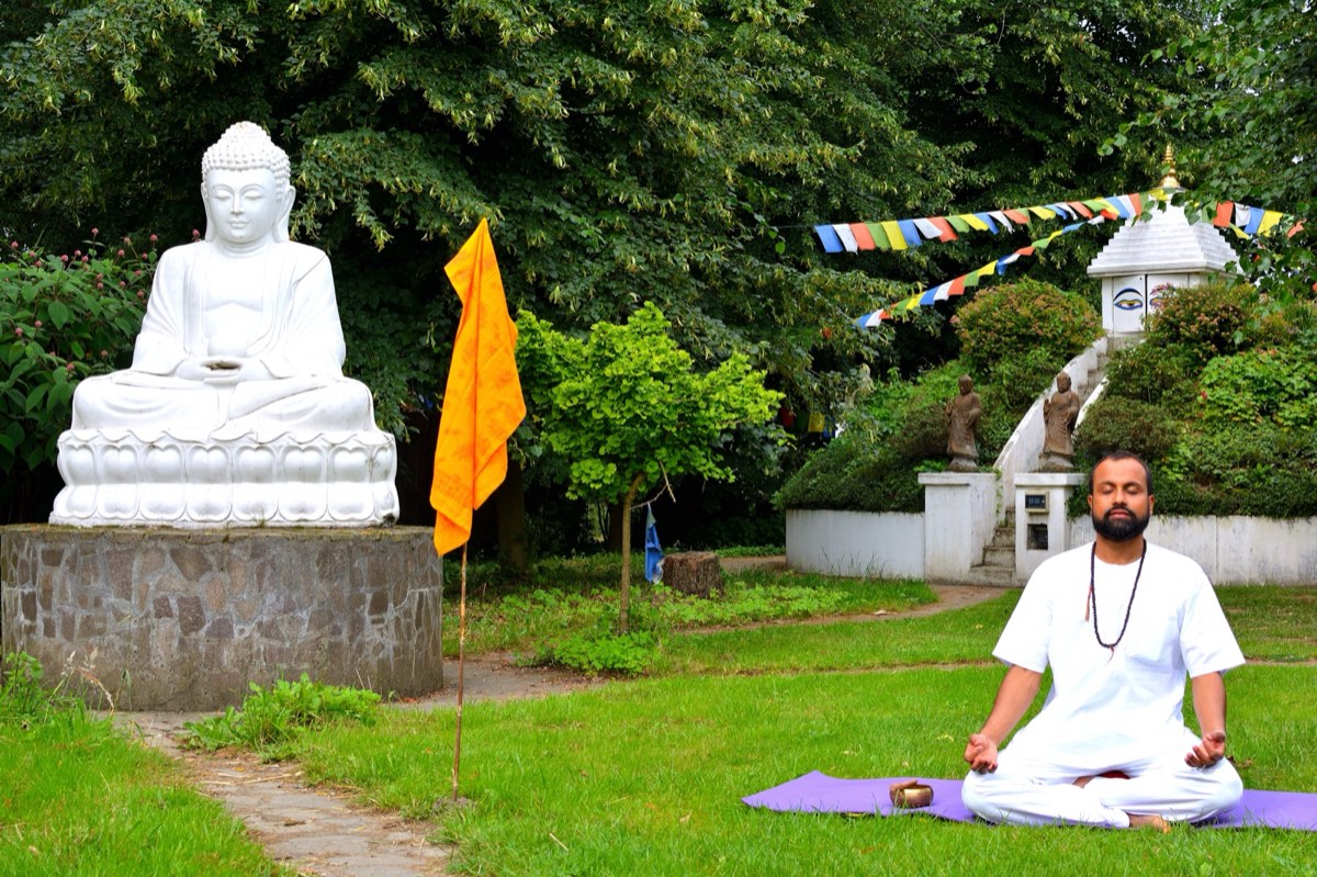 Anup meditiert in einem Garten vor einer weißen Buddha-Statue